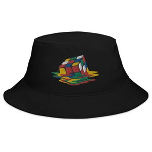 May include: Black bucket hat featuring an embroidered design of a melting Rubik's Cube. The cube's colors include red, blue, yellow, green, and white, with the melted portions flowing down the hat. The hat is made of a soft, durable fabric.