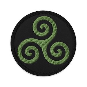 Op de afbeelding: Een zwarte ronde patch met een groen geborduurd Keltisch triskelion-symbool.
