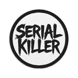 May include: Embroidered patch with the words "SERIAL KILLER" in bold, black, distressed lettering. The text is centered on a white circle, framed by a black border. The patch is round and likely designed to be sewn or ironed onto fabric.