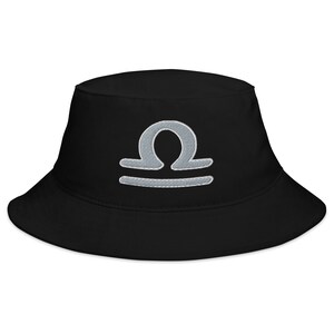 Puede incluir: Sombrero de pescador negro con un símbolo de Libra del zodíaco bordado en plata.