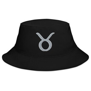 Puede incluir: Sombrero de pescador negro con un símbolo de Tauro del zodíaco bordado en plata.