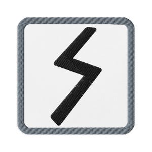 May include: Embroidered patch featuring a black zig-zag symbol on a white background. The patch has a square shape with a gray denim-like border. The design is simple and bold, suitable for various applications.