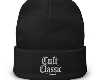 Può includere: Berretto nero con la scritta "Cult Classic" ricamata in bianco. Il berretto è in stile classico, con risvolto. Il testo è in un carattere gotico.