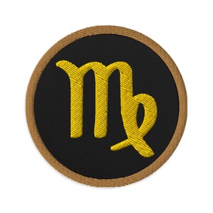 May include: Embroidered patch featuring the Virgo zodiac symbol in gold thread on a black circular background. The patch has a brown border. This patch is suitable for clothing, bags, or other fabric items.