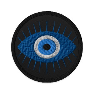 May include: A blue evil eye with a white circle and black pupil, embroidered on a black circular patch.
