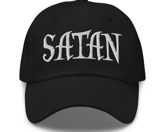Puede incluir: Gorra de béisbol negra con la palabra "SATAN" bordada en blanco. La gorra tiene una visera curva y un botón en la parte superior. El texto está en una fuente de estilo gótico.
