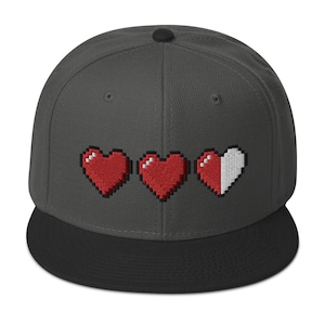 May include: A dark gray and black baseball cap with a pixelated heart design. The hearts are red and white, with one heart partially filled in.