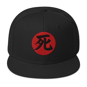 Puede incluir: Gorra de béisbol negra con visera plana. Un círculo rojo con un carácter Kanji japonés está bordado en la parte delantera. La gorra está hecha de una tela duradera y tiene un ajuste estructurado.
