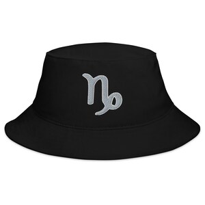 Puede incluir: Sombrero de pescador negro con un símbolo de Capricornio bordado en plata.