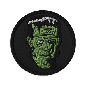 May include: A black and green embroidered patch featuring a cartoon image of Frankenstein's monster.