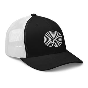 May include: A black and white trucker hat with a white embroidered labyrinth design on the front. The hat has a black front panel and a white mesh back panel.