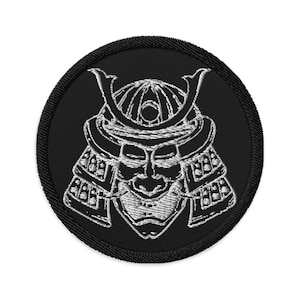 Puede incluir: Un parche bordado negro con un contorno blanco de un casco y una cara de samurai.