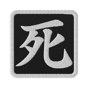 May include: A square embroidered patch with a black background and a white border. The centre features the white Japanese kanji character for death, which is written in a bold, stylized script with thick, textured embroidery stitching.