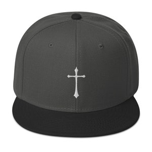 May include: A dark gray and black baseball cap with a white embroidered cross on the front.