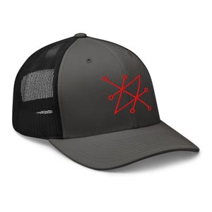 May include: A black and grey trucker hat with a red geometric design embroidered on the front. The hat has a mesh back.
