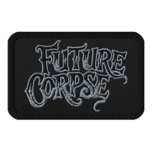 May include: A black rectangular patch featuring the embroidered words "FUTURE CORPSE" in a light grey, stylized font. The patch has a black border and a textured finish.