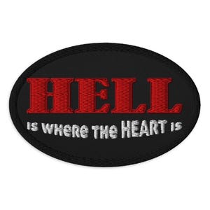May include: Black oval patch with the embroidered text "HELL" in red, above the phrase "IS WHERE THE HEART IS" in white. The patch has a black border.
