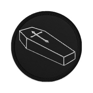 Könnte beinhalten: Schwarzer gestickter Aufnäher mit einem weißen Umriss eines Sarges mit einem Kreuz darauf.