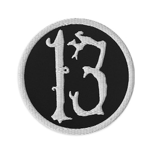 May include: A white embroidered patch with the number "13" in a stylized font on a black circular background. The patch has a white border.