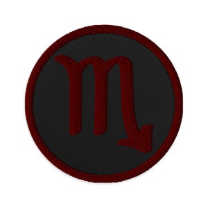 May include: A black and red embroidered patch with the astrological symbol for Scorpio, a stylized letter "M" with a downward arrow.