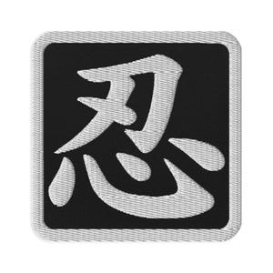 Peut inclure: Un écusson brodé carré présentant un fond noir avec une bordure blanche et le caractère kanji japonais blanc pour ninja, qui est 'nin', centré de manière proéminente au milieu de l'écusson avec un aspect de fil cousu texturé.