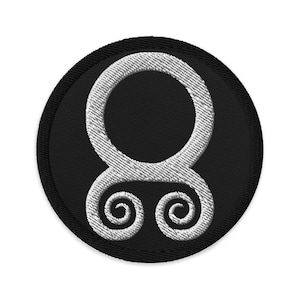 May include: A black and white embroidered patch with a circular design. The design features a white circle with two white swirls at the bottom.