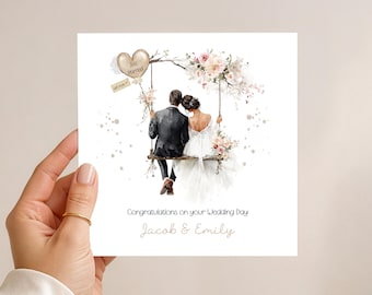 May include: A wedding card featuring a watercolor illustration of a couple on a swing adorned with flowers. The card includes the text "Just Married" on a heart-shaped balloon and "Congratulations on your Wedding Day" with the names "Jacob & Emily".