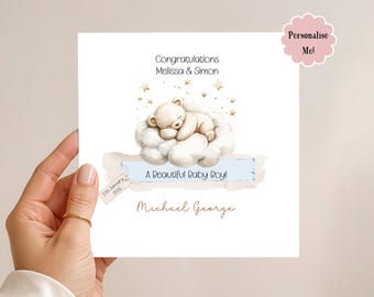 May include: A square white card with a baby-themed illustration. It features a sleeping teddy bear on a cloud, with text reading "Congratulations Melissa & Simon" and "A Beautiful Baby Boy!". The card is personalised.