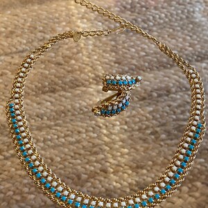 Puede incluir: Un collar y pendientes de oro con un dise&ntilde;o de esmalte azul y blanco. El collar es una cadena con cuadrados de esmalte azul y blanco alternados. Los pendientes son peque&ntilde;os aros con el mismo dise&ntilde;o de esmalte azul y blanco.