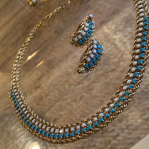 Puede incluir: Un collar de cadena dorada con detalles de esmalte azul y blanco. El collar se combina con pendientes a juego.