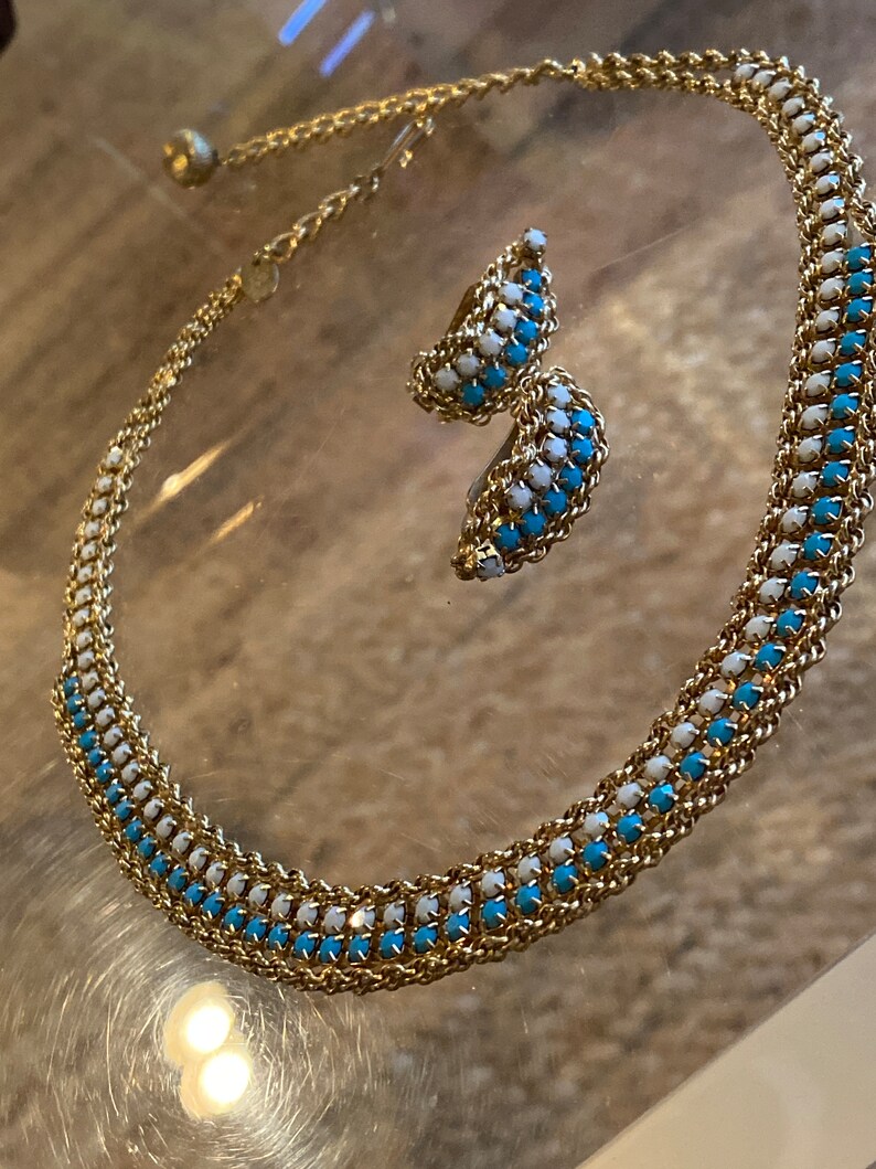 Puede incluir: Un collar de cadena dorada con detalles de esmalte azul y blanco. El collar se combina con pendientes a juego.
