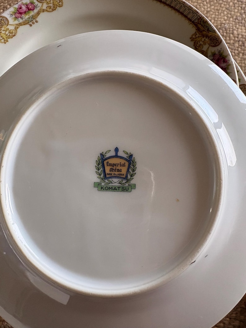 May include: White porcelain plates with floral and gold trim. The underside of the plate features the text "Imperial China Made in Japan" and the name "KOMATSU" in a green rectangle.