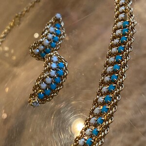 Puede incluir: Un collar de cadena de oro con cuentas azules y blancas alternadas. El collar se combina con un par de pendientes a juego.