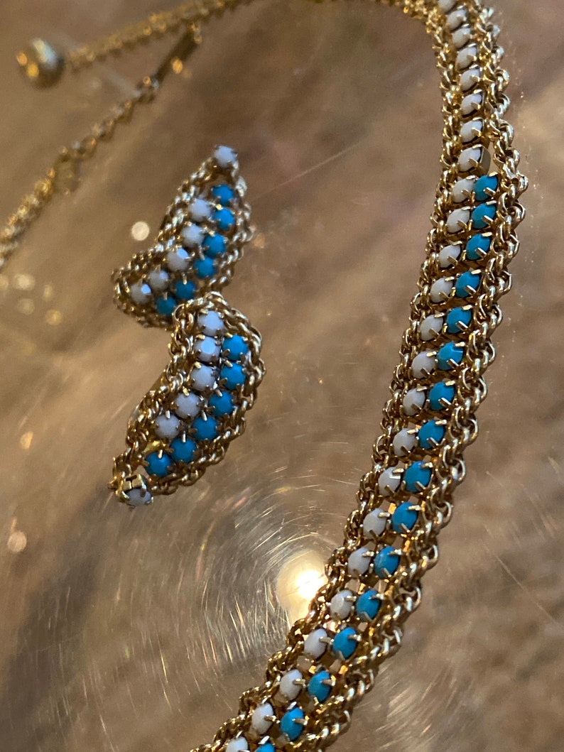 Puede incluir: Un collar de cadena de oro con cuentas azules y blancas alternadas. El collar se combina con un par de pendientes a juego.