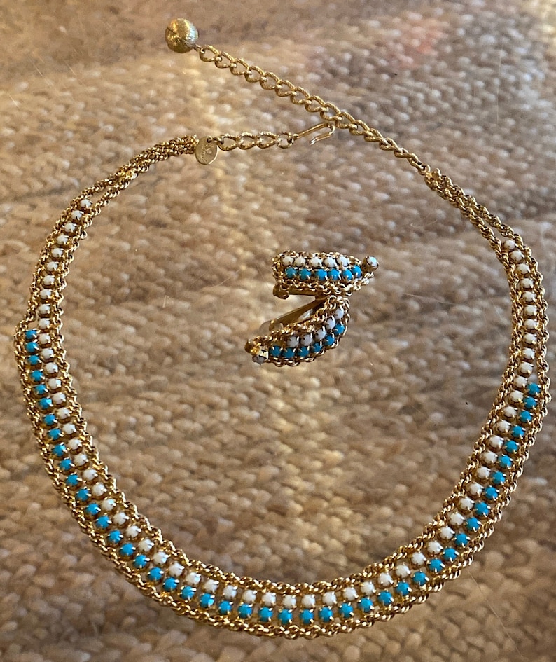 Puede incluir: Un collar y pendientes de oro con un dise&ntilde;o de esmalte azul y blanco. El collar es una cadena con cuadrados de esmalte azul y blanco alternados. Los pendientes son peque&ntilde;os aros con el mismo dise&ntilde;o de esmalte azul y blanco.