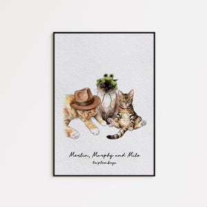 May include: Watercolor print of three cats, each with unique accessories. One cat wears a brown fedora, another a frog hat, and the third sits upright. The print is framed and features the text "Merlin, Murphy and Milo tripleboys."