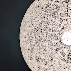 May include: A white string globe light fixture with a single light bulb hanging from a red cord.