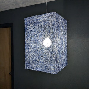 May include: A blue and white string light fixture with a square shape. The light fixture is hanging from the ceiling and is turned on, illuminating the room.