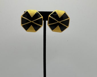 May include: A pair of gold-tone earrings with black geometric designs. The earrings are octagonal in shape and have a raised, textured surface.