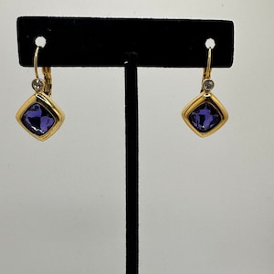 May include: A pair of gold earrings with a square-shaped purple gemstone and a small clear rhinestone accent.