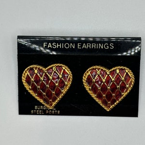 May include: A pair of heart-shaped earrings with a red and gold lattice design. The earrings are on a black card with the text "FASHION EARRINGS" and "SURGICAL STEEL POSTS".
