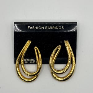 May include: Gold-toned double hoop earrings with a textured finish. The earrings are on a black card with the text "FASHION EARRINGS" and "SURGICAL STEEL POSTS".