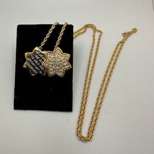 May include: A gold chain necklace with two pendants. One pendant is a star with the words "Let your star hold on to what your destiny is" and the other pendant is a flower with clear rhinestones.