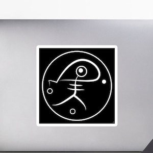 May include: A white sticker with a black square design featuring a stylized, minimalist figure within a white circle. The figure resembles a fish-like form with a large eye and a small circle on each side. The sticker is on a laptop.