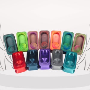 May include: A selection of vibrantly coloured soap dishes, including red, blue, green, and purple. Each rectangular dish has a circular soap holder and a textured surface. The soap dishes are presented on a white platform.