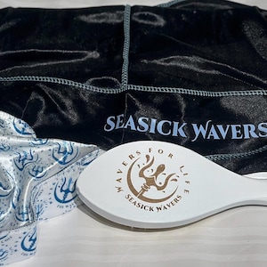 May include: A white wooden brush with a brown logo that says "Wavrs For Life 4 Seasick Wavrs 3". The brush is on a white surface next to a black satin headband with the text "Seasick Wavrs" in white and a white satin hair scarf with a blue and white pattern.
