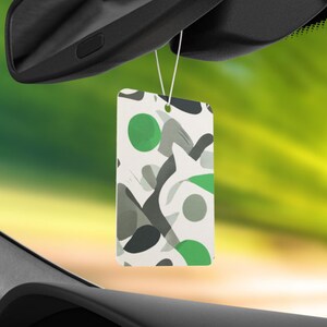 Peut inclure: Un diffuseur d'air de voiture blanc avec un motif g&eacute;om&eacute;trique dans des tons de vert, gris et blanc. Le diffuseur d'air est suspendu au r&eacute;troviseur d'une voiture.