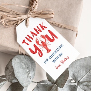 May include: A gift wrapped in brown paper, tied with raffia, and adorned with a white tag. The tag features the words "THANK YOU" in red, a red lobster illustration, and the message "FOR CELEBRATING WITH US!" in blue, signed "love, Shelby."