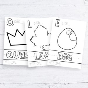 Może przedstawiać: Trzy białe karty z czarnymi konturami korony, liścia i jajka. Na kartach napisano "Q is for Queen", "L is for Leaf" i "E is for Egg". Fraza "With Love" jest wydrukowana na dole każdej karty. Karty leżą na białej drewnianej powierzchni.