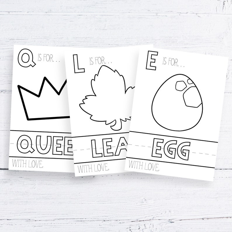 Może przedstawiać: Trzy białe karty z czarnymi konturami korony, liścia i jajka. Na kartach napisano "Q is for Queen", "L is for Leaf" i "E is for Egg". Fraza "With Love" jest wydrukowana na dole każdej karty. Karty leżą na białej drewnianej powierzchni.